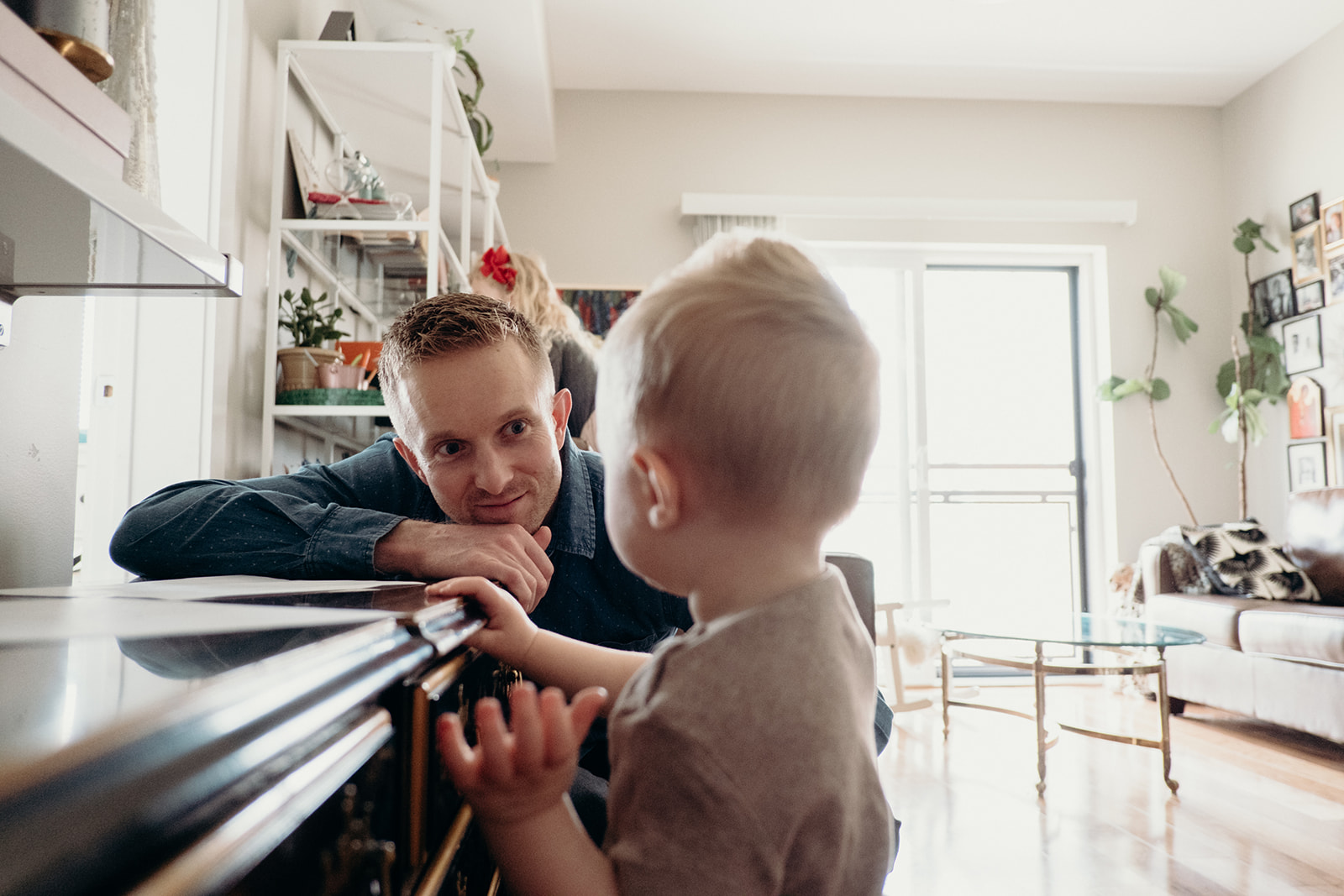 A father looks on while his son makes a drawing on paper in their apartment in Washington, DC.