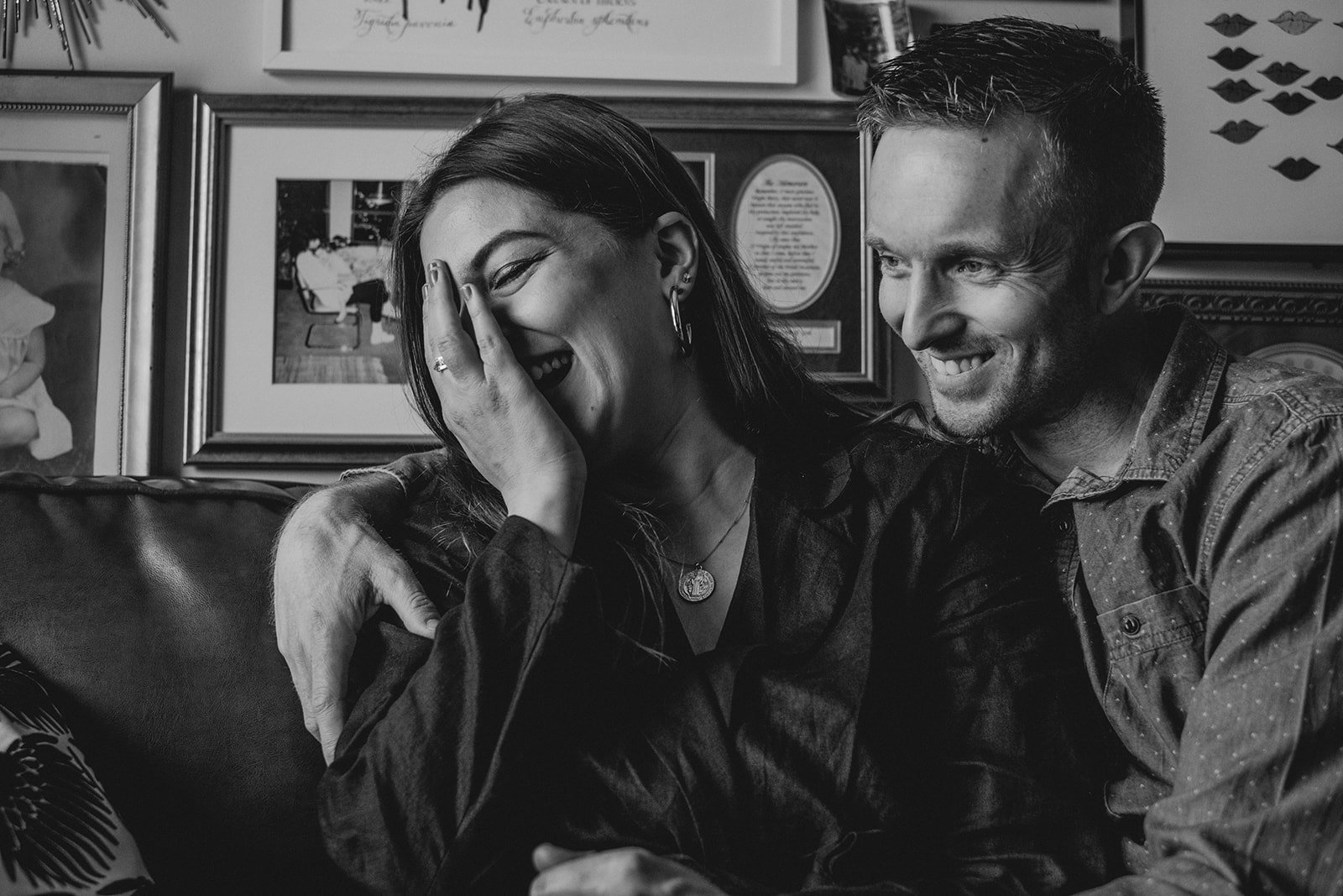 A woman covers her face while laughing and sitting next her her husband on a couch in their apartment in Washington, DC.