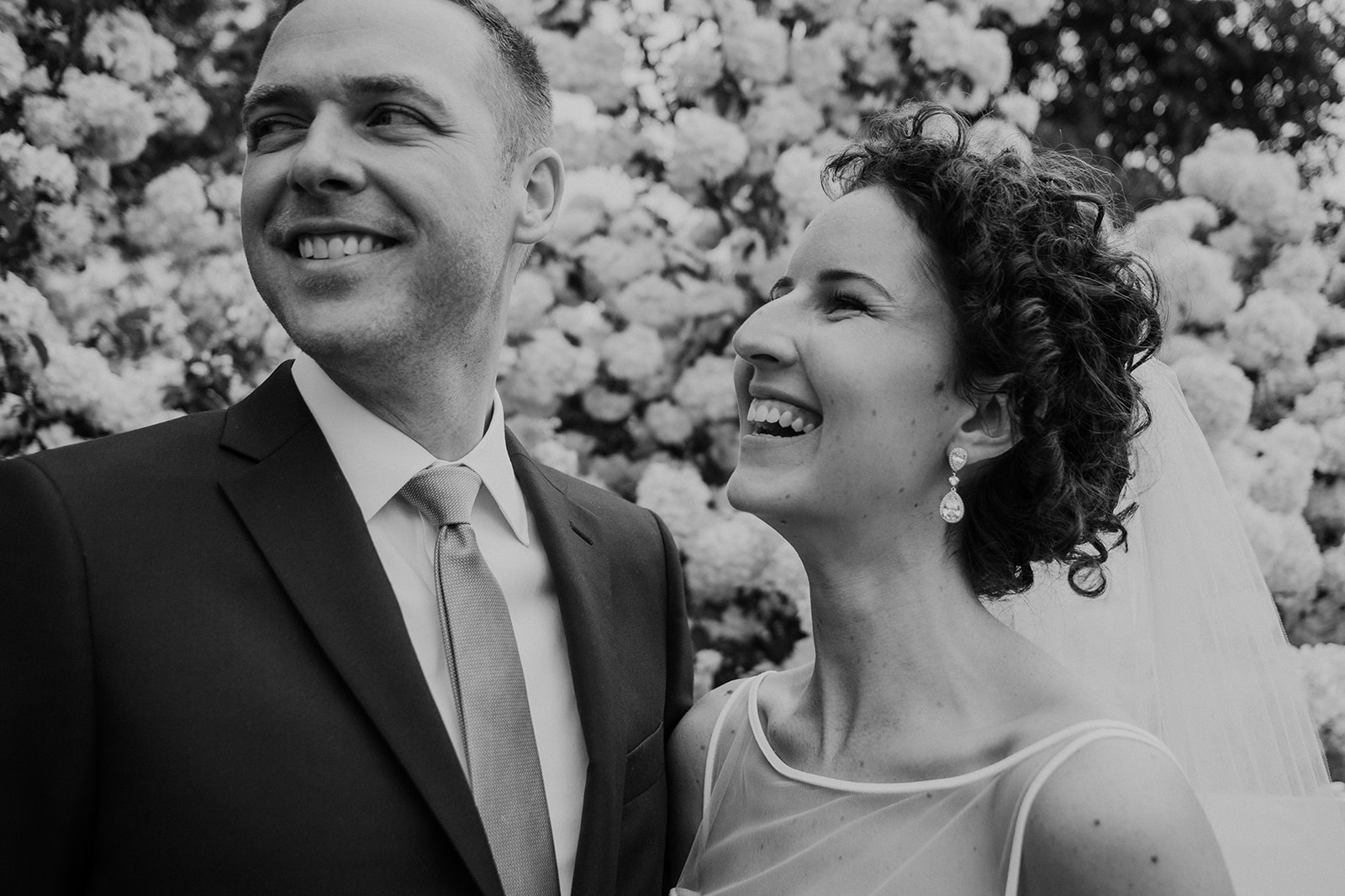 A bride looks at her groom in front of a large flowering bush at Blue Hill Farm in Waterford, VA. 