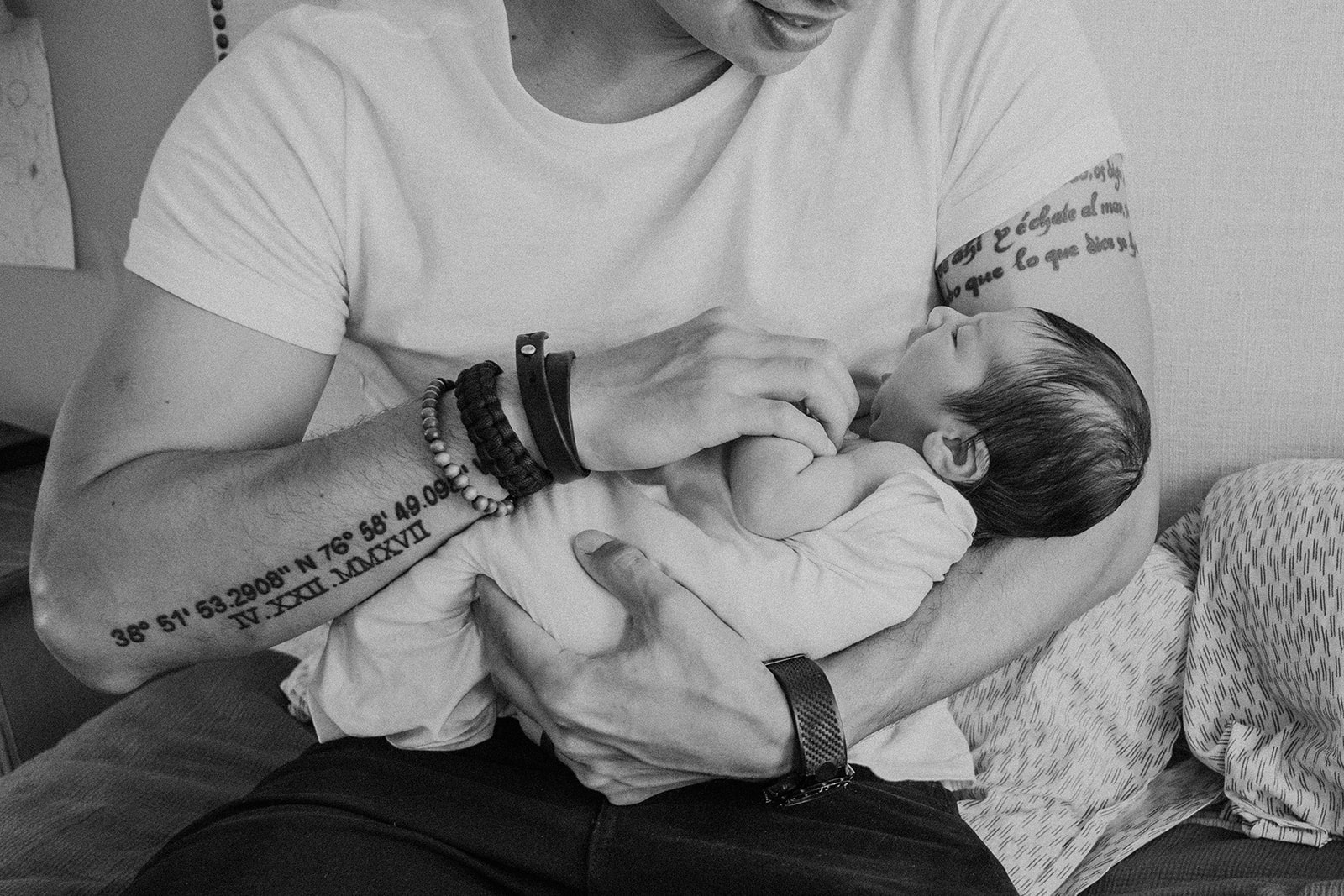 A tattooed father holds his newborn son during an in home family photography session. 