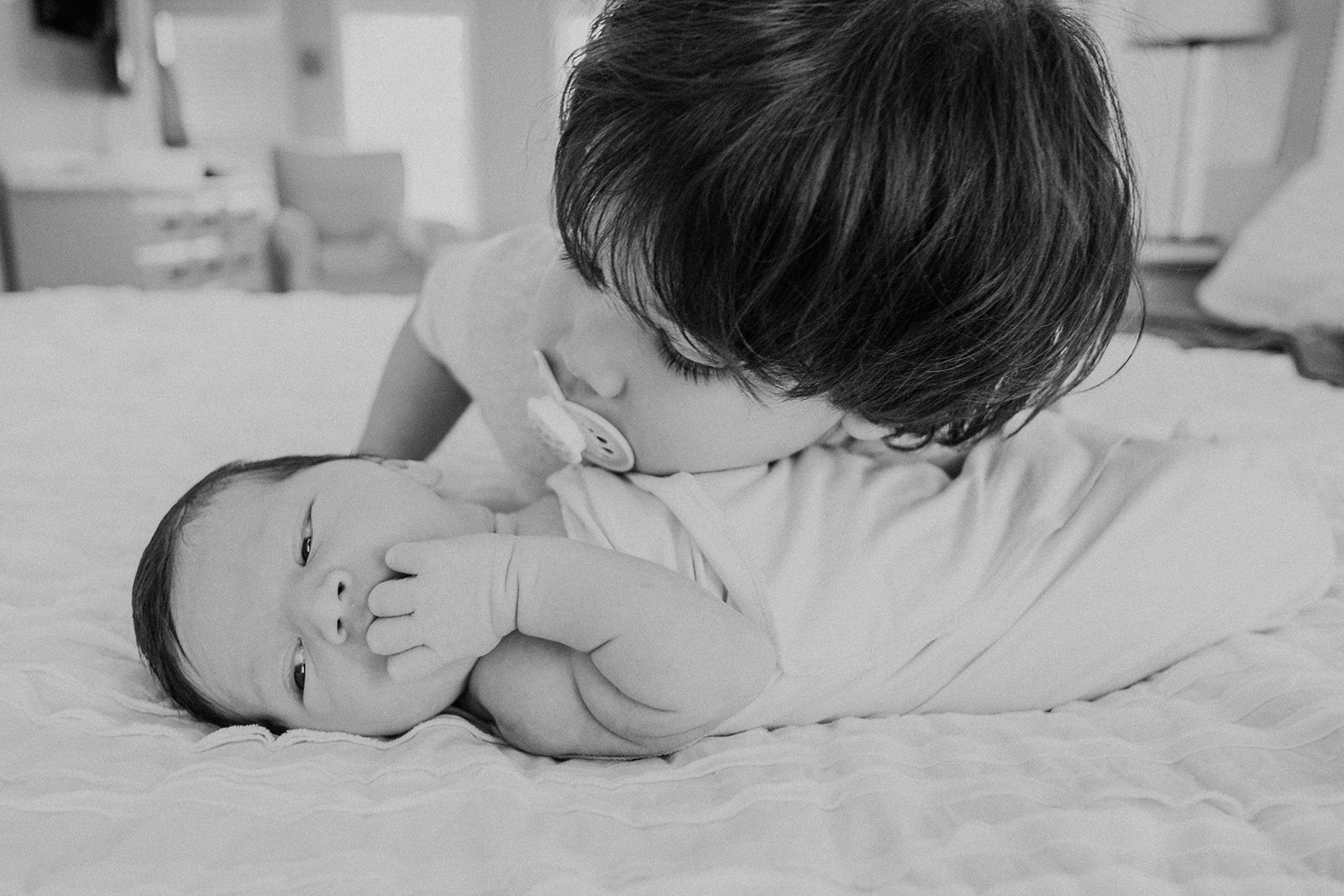 A little boy looks at his newborn baby brother during an in-home family photography session.