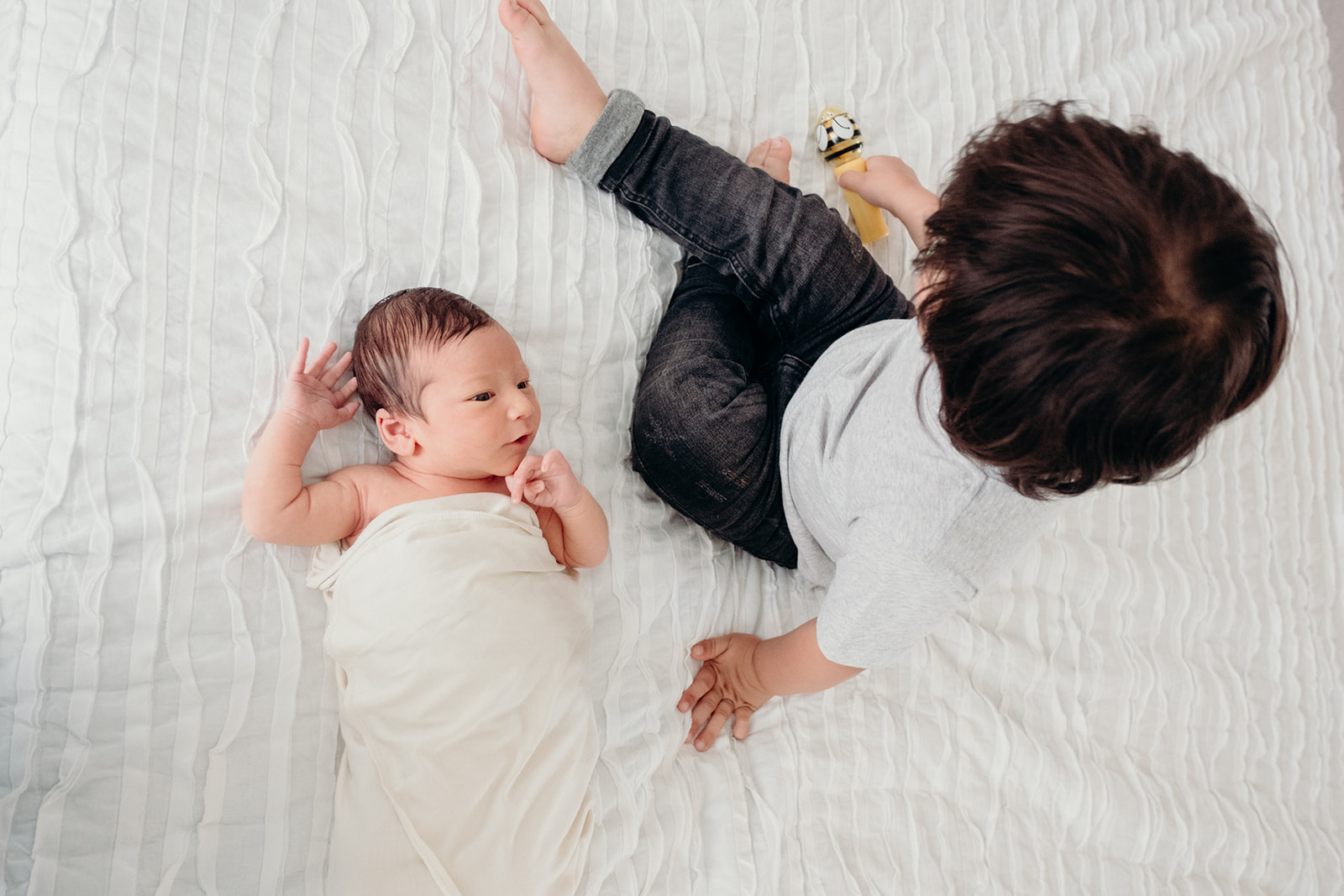 A little boy sits next to his newborn baby brother during an in home family photography session. 