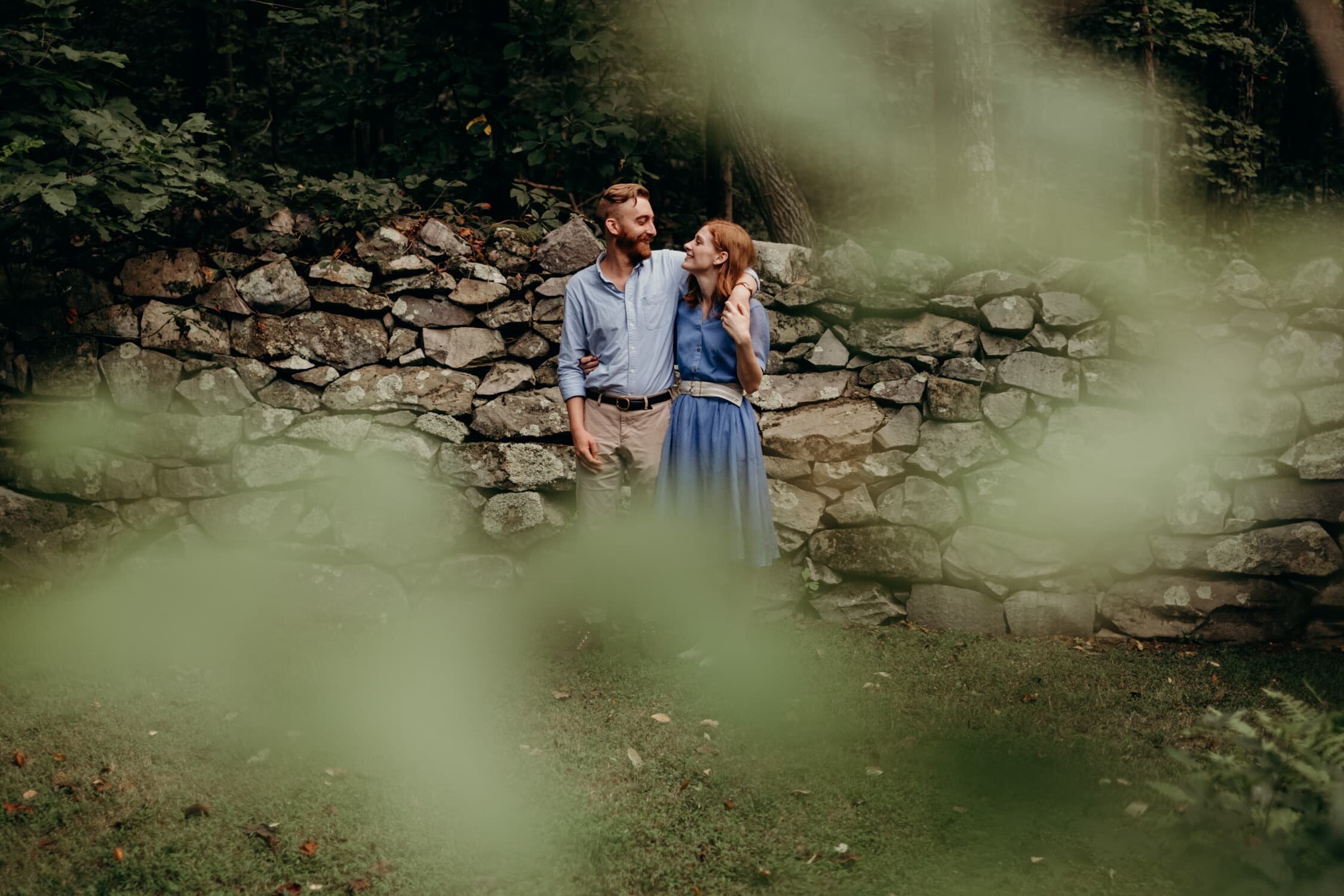 Engaged couple standing in front of a rock wall