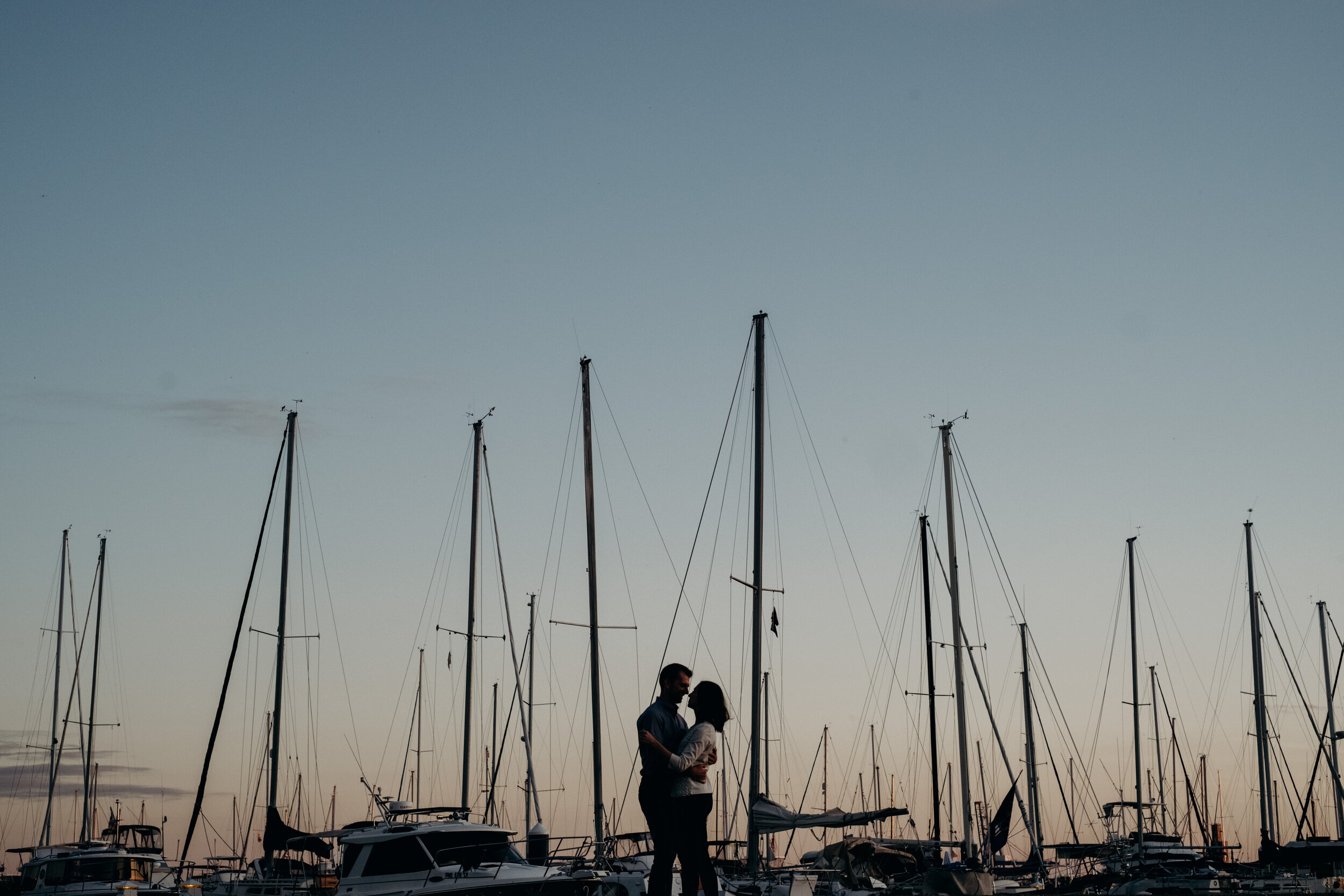 An engaged couple is silhouetted in the sunset over the Inner Harbor in Baltimore, MD. 