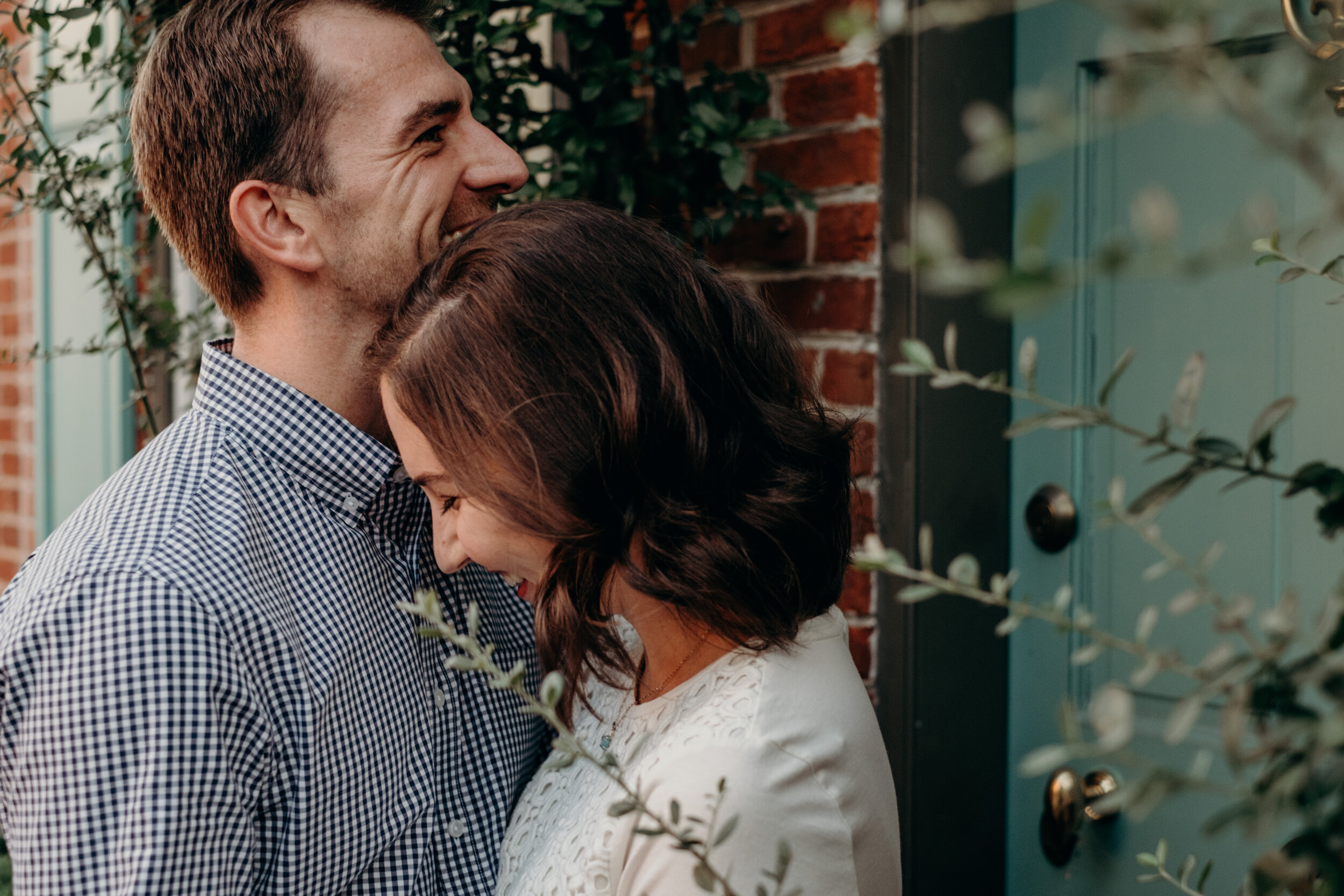 An engaged couple laughs near a brick wall in Baltimore, MD during an engagement photo session. 