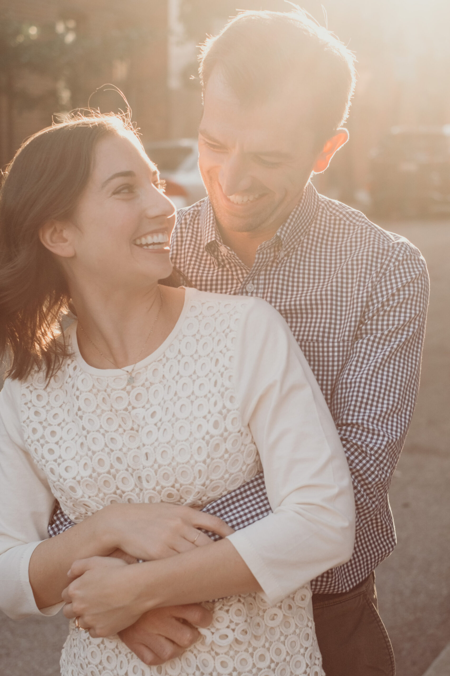 An engaged couple smiles at one another during sunset on the streets of Baltimore, MD.