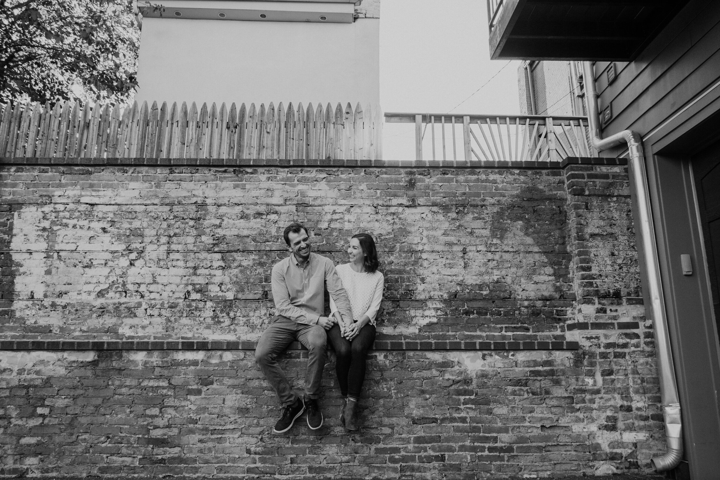 A couple sits together on a ledge on a brick wall in the city of Baltimore, MD.