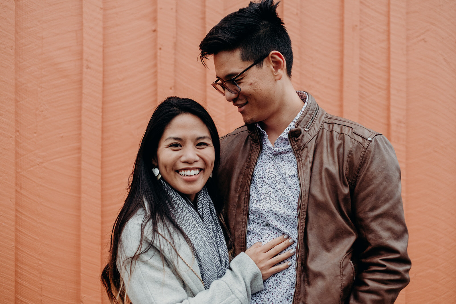 A woman looks directly at the camera while her fiancé looks at her during their engagement photo session in downtown Leesburg, VA.