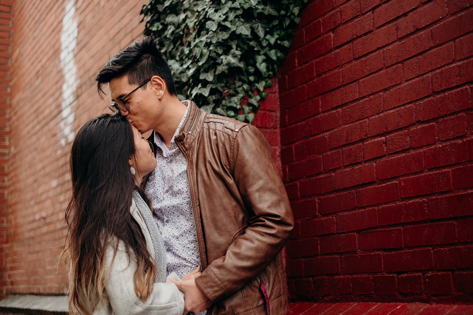 A man kisses his fiancé's forehead in an ivy-lined alley in downtown Leesburg, VA during their engagement photo session. 