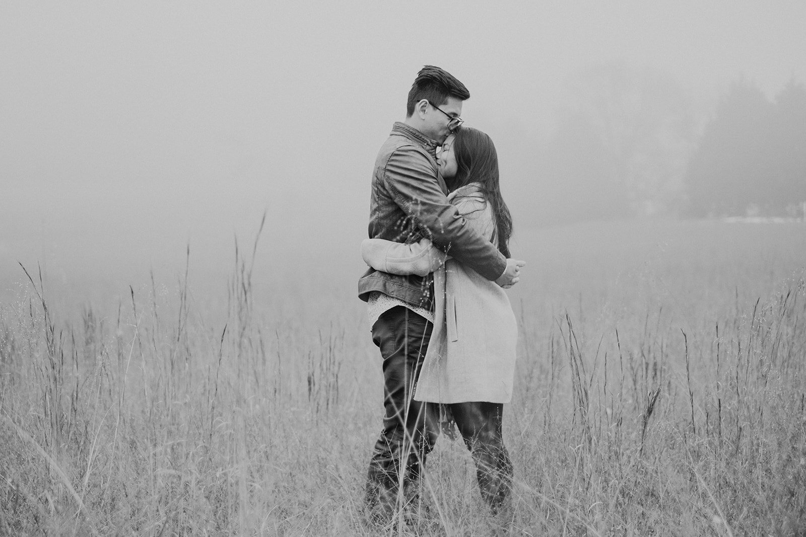 An engaged couple holds one another in a grassy, foggy field in Morven Park in Leesburg, VA during their engagement photo session. 