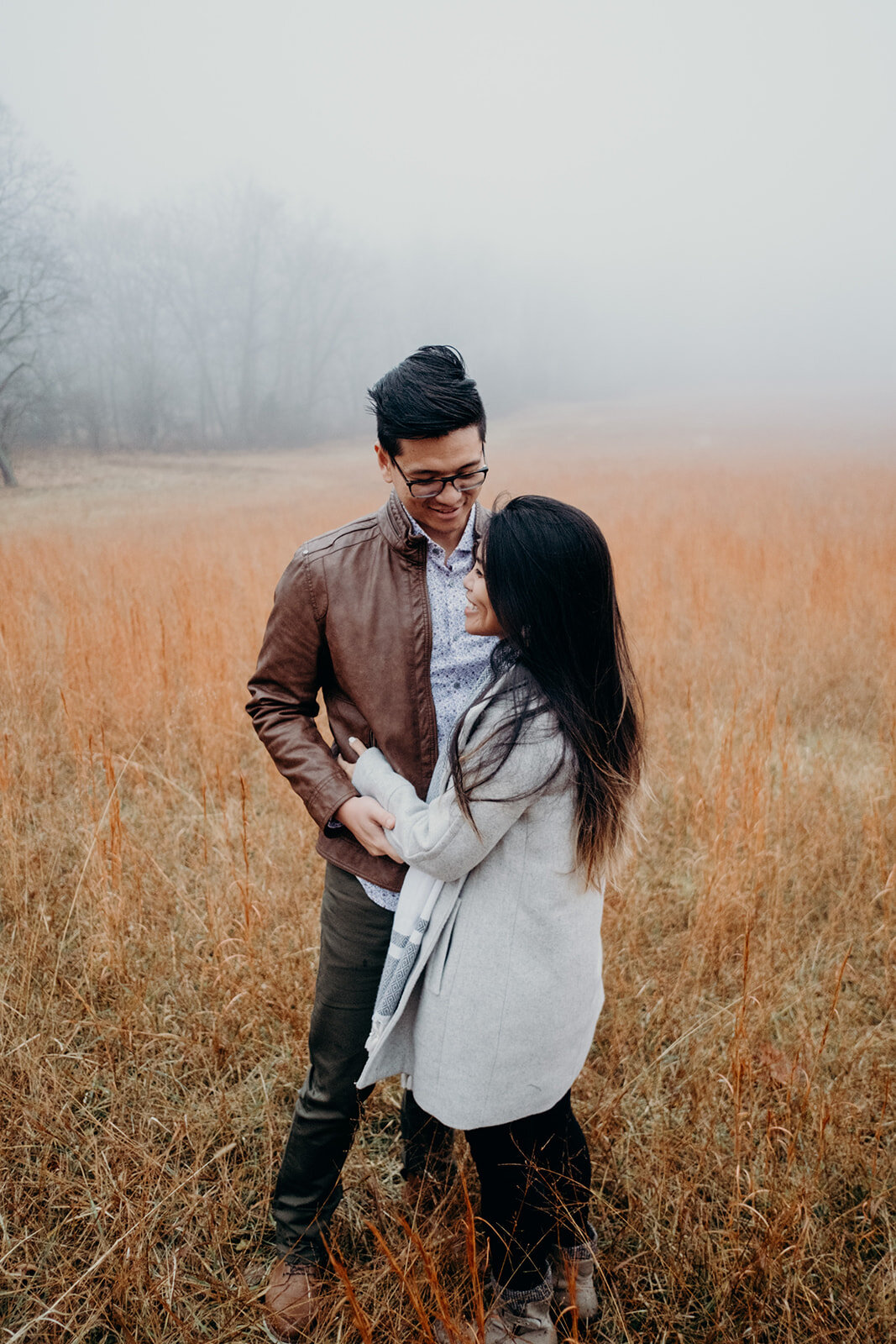 A man looks at his fianceé as she looks out over the grassy, foggy field in Morven Park in Leesburg, VA during their engagement photo session.