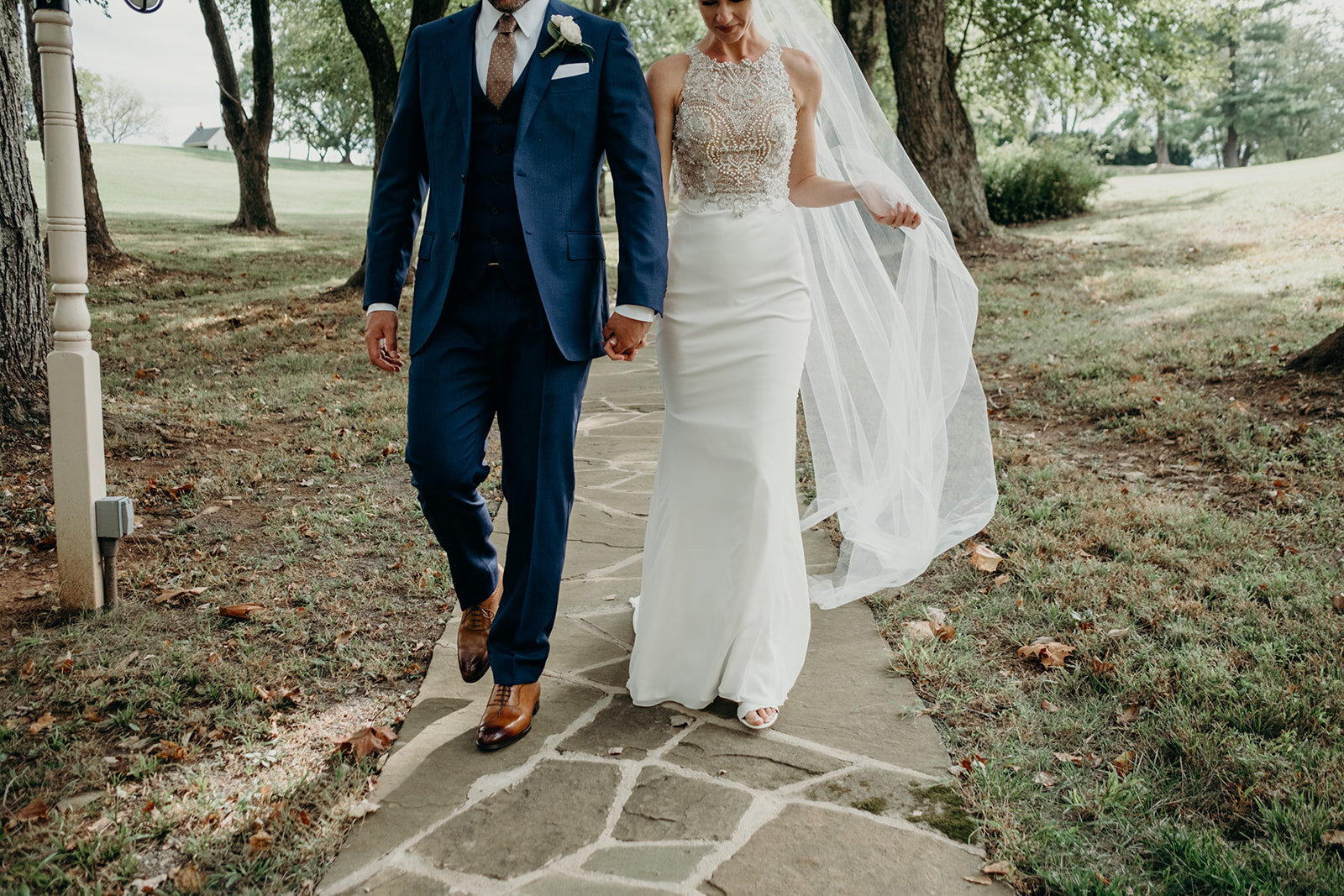 A bride and groom hold hands while walking down a pathway at the Retreat at Eastwood Farm in Warrenton, VA. 