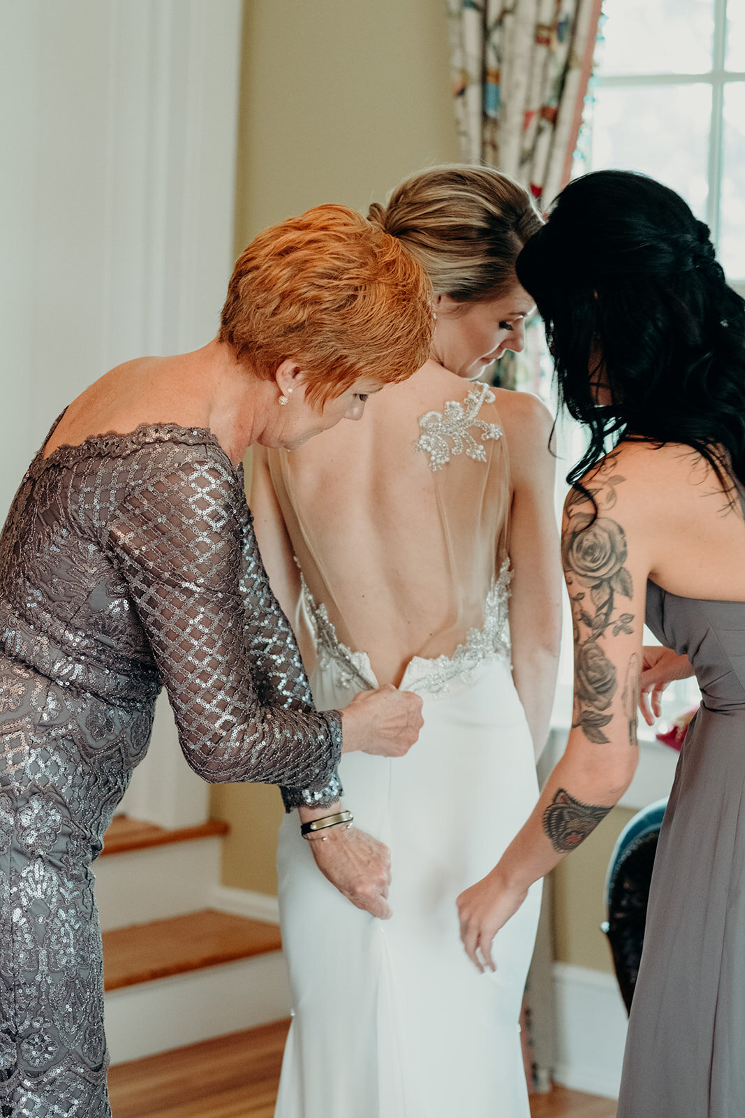 A bride is helped by her mother and sister into her wedding dress before her outdoor garden wedding at the Retreat at Eastwood in Warrenton, VA.