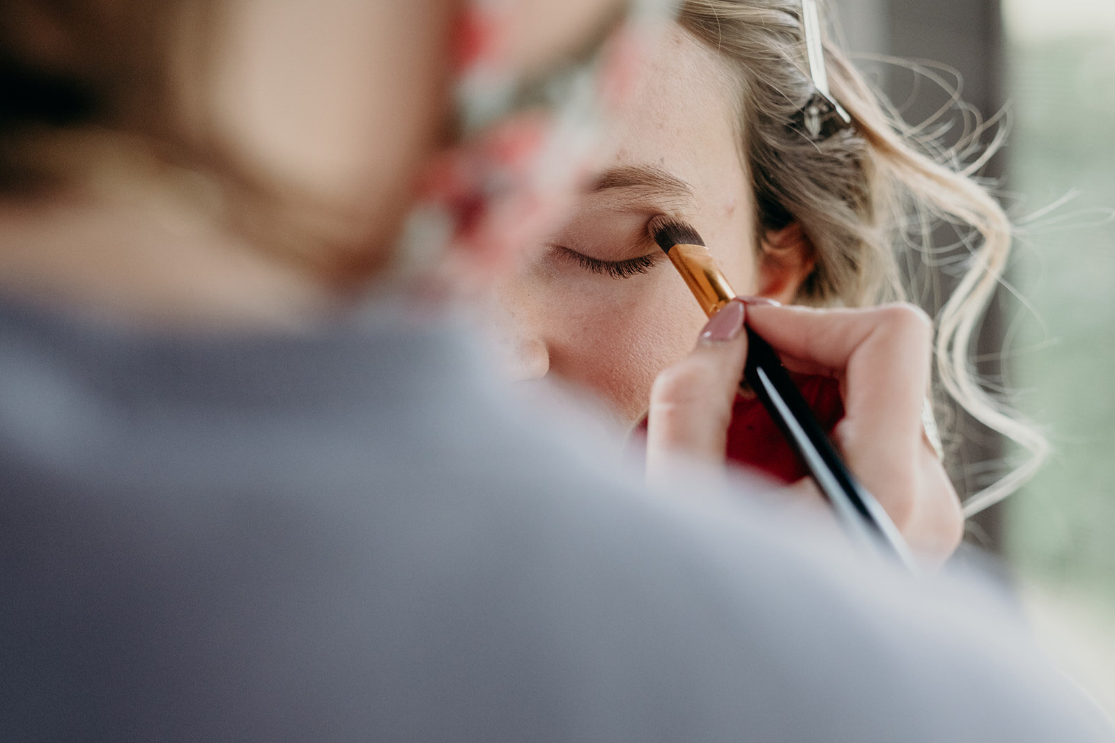 Eyeshadow is put on the sister of the bride during getting ready for the outdoor farm wedding ceremony. 