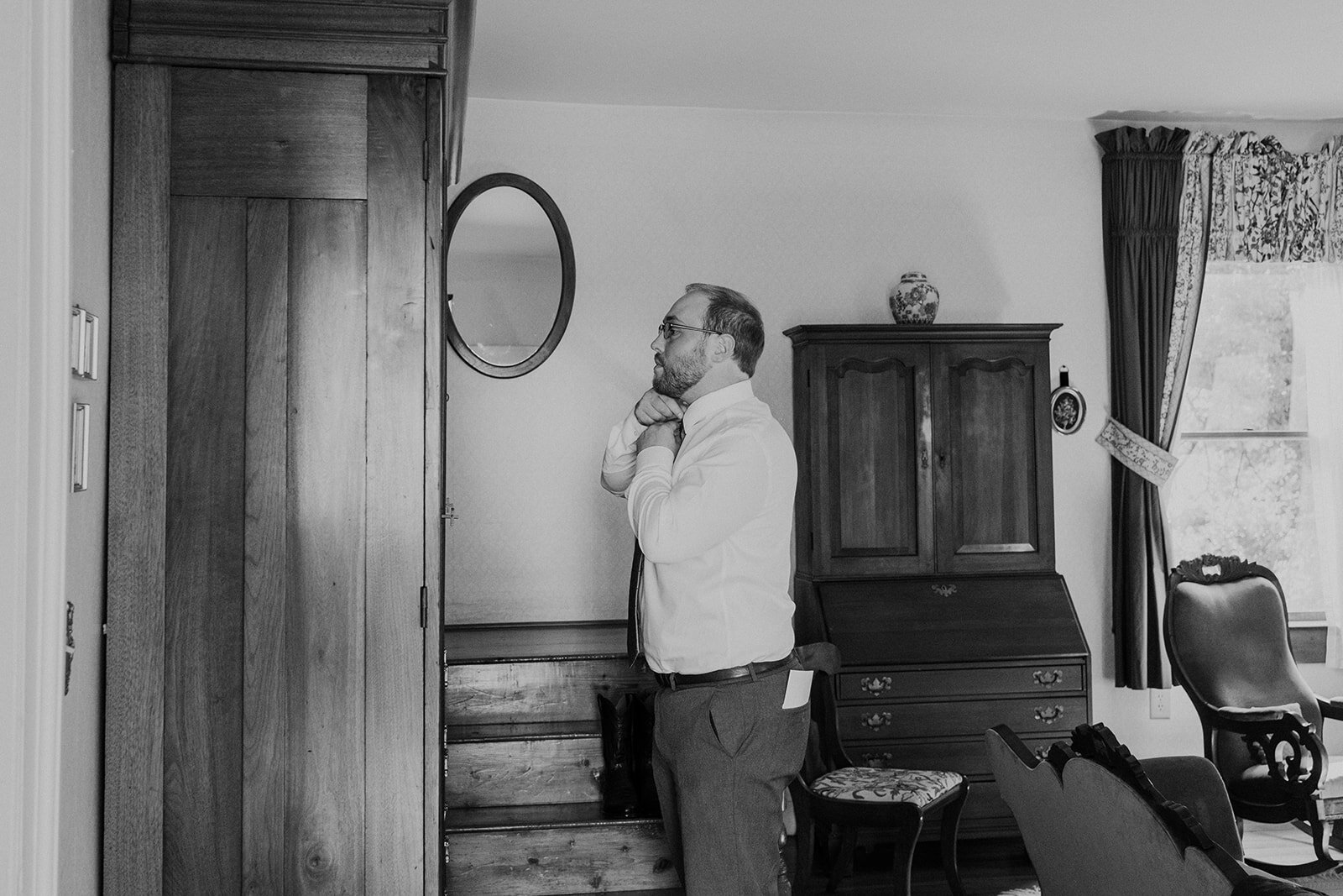 A friend of the groom adjusts his tie before officiating an outdoor farm wedding ceremony.