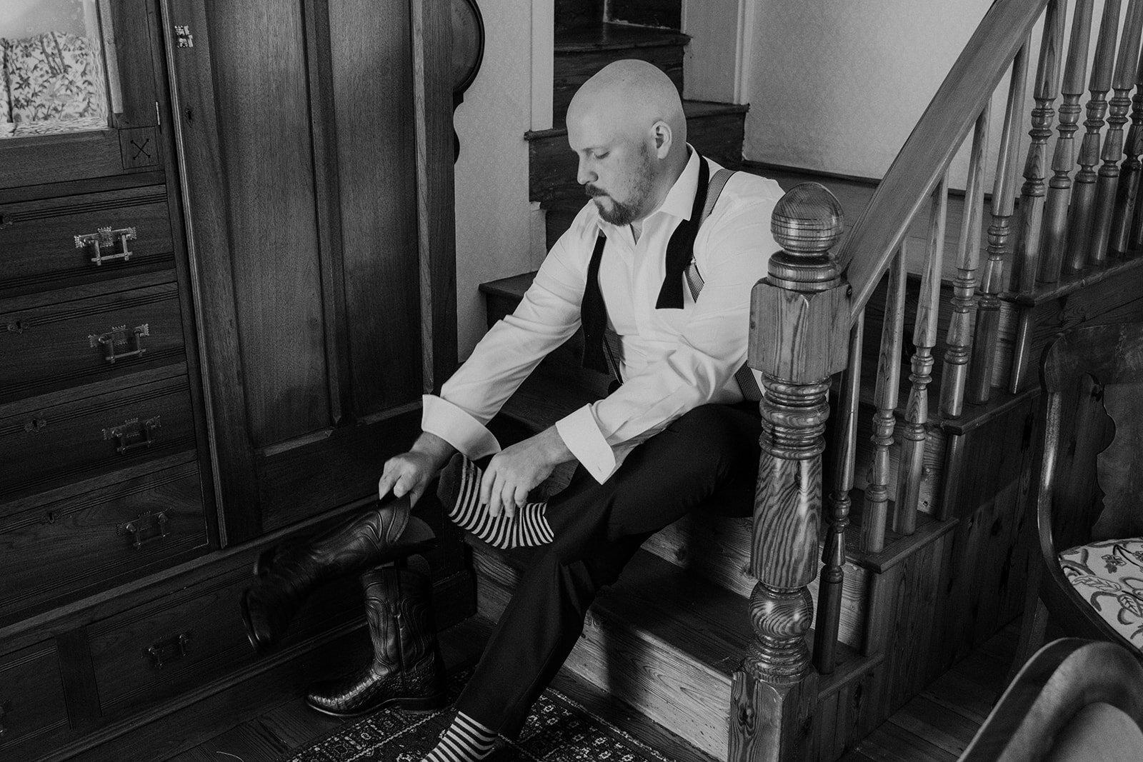 The groom puts on his black cowboy boots before his outdoor farm wedding ceremony.