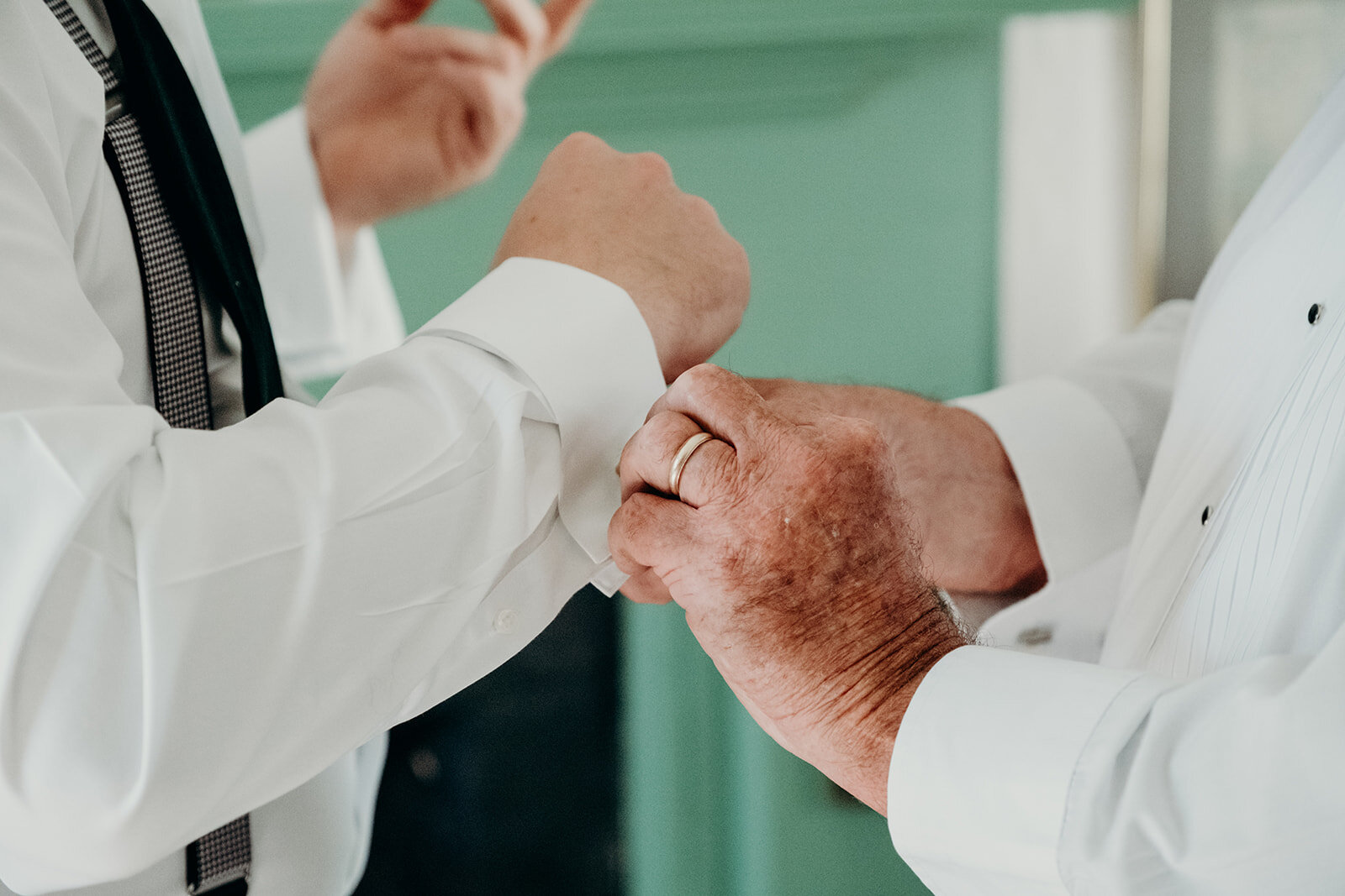 The father of the groom helps him adjust his cufflinks as he gets ready for his outdoor wedding.