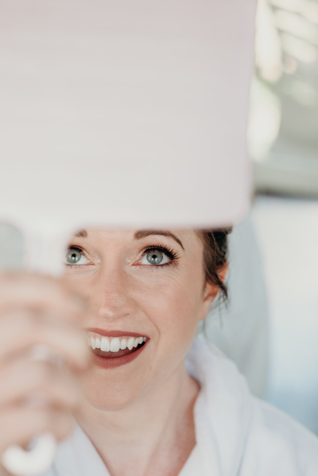 A bride is overjoyed checking her hair and makeup before her outdoor farm wedding ceremony. 