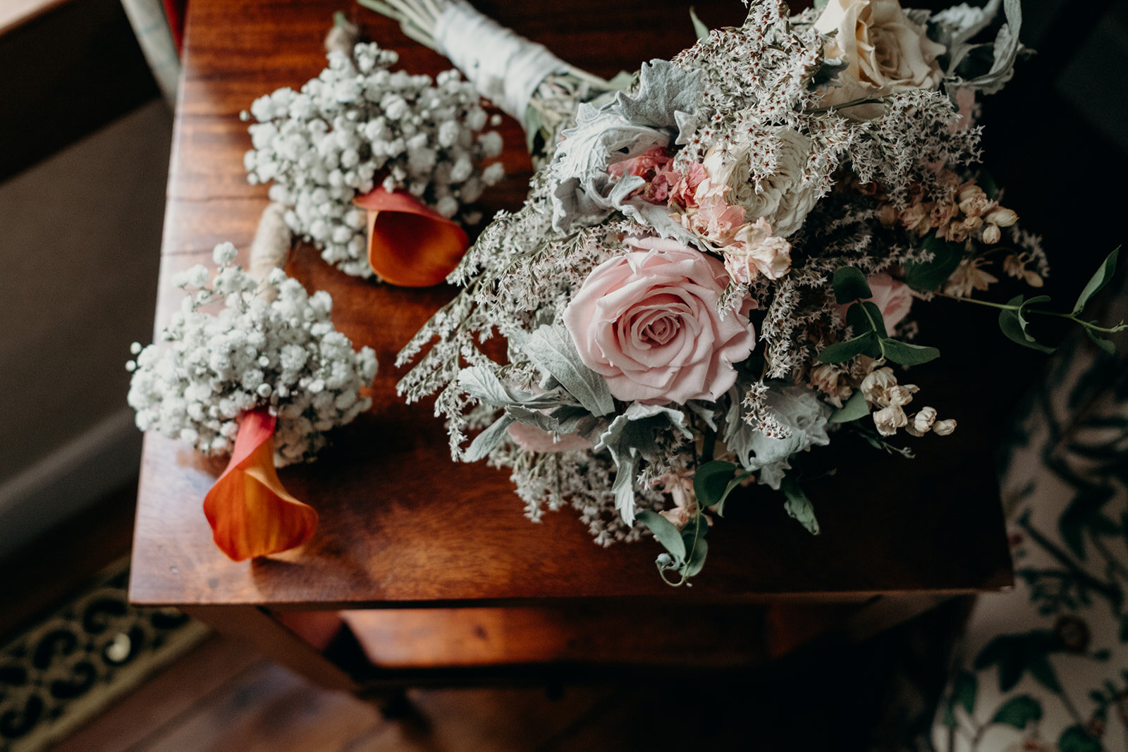 A bridal bouquet made of dried flowers sits next to two smaller bouquets for the bridesmaids with baby's breath and orange calla lilies. 