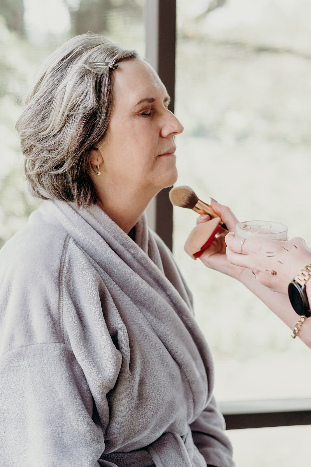 The mother of the bride gets her makeup done before the outdoor farm wedding ceremony.